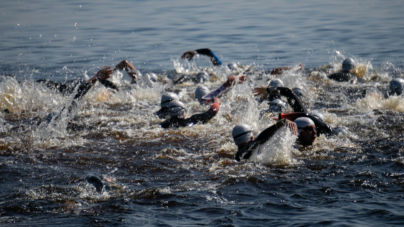Triathleter i våtdräkt simmar i grått, oroligt vatten